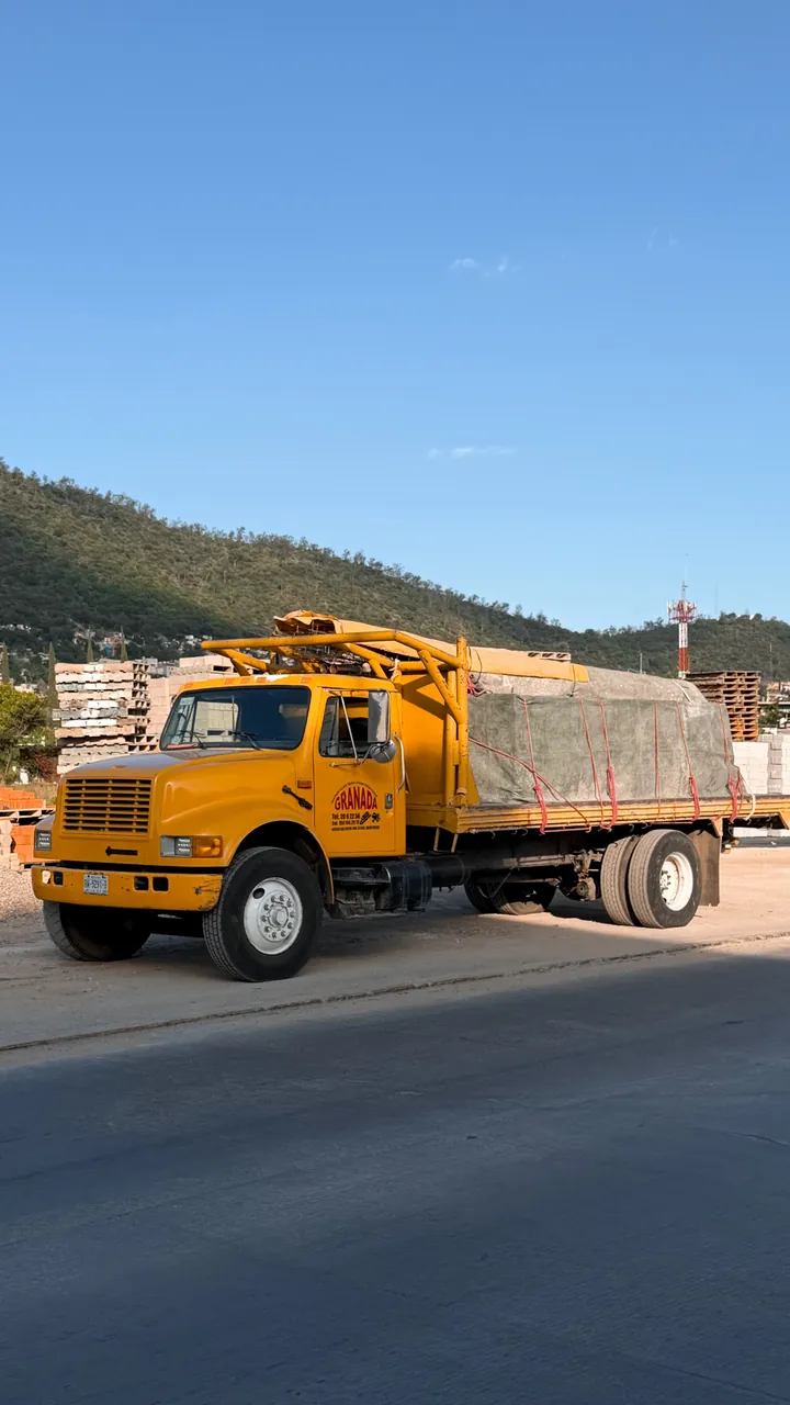 Camión amarillo de Materiales Granada con carga cubierta, frente al patio de materiales